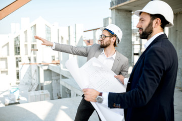 Two business men or engeneers working with house drawings on the structure during the construction...