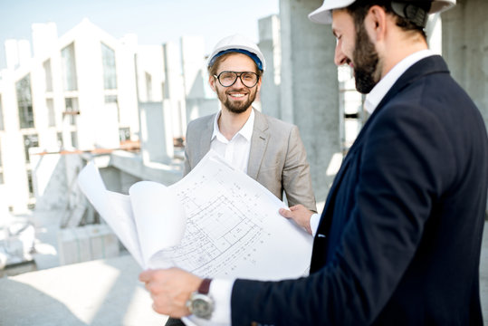 Two business men or engeneers working with house drawings on the structure during the construction process outdoors