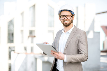 Handsome engineer working with tablet standing on the structure site with a new house on the...