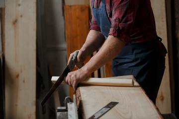 Master carpenter saws board with hacksaw in workshop. Close up