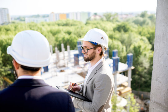 Two engineers or architects supervising the process of residential building construction standing on the structure outdoors