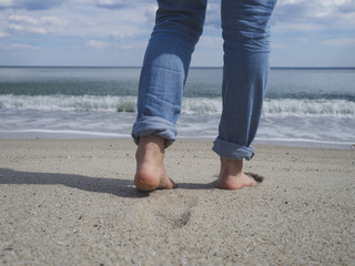 Woman's bare feet walking on a beautiful sandy beach towards the water