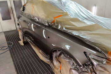 Painting the car in the workshop for body repair. Car covered with paper from hitting paint.