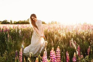 Young long-hair woman walking on flower field at sunset on background. Horizontal view with copy space