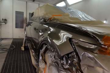Painting the car in the workshop for body repair. Car covered with paper from hitting paint.