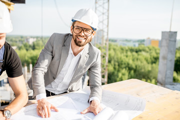 Portrait of a handsome engineer working with architectural drawings at the table on the construction site outdoors