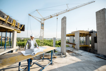 Handsome engineer working with architectural drawings at the table on the construction site outdoors - Powered by Adobe