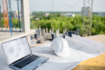 Workspace with architectural drawings laptop and protective helmet at the table on the construction...
