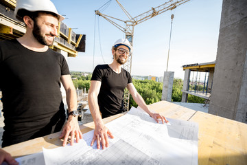 Two workers in black t-shirts and protective harhats working with drawings at the construction site...