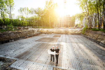 Wide angle view on the concrete foundation at the construction site with two builders standing with...