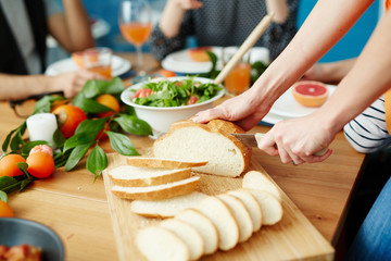 Crop close-up hands cutting white bread at dining table while eating together with friends