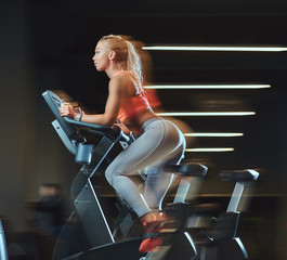 Fototapeta na wymiar Sportive blonde woman working out on an exercise bike in modern fitness center. Fitness lifestyle in sport club.