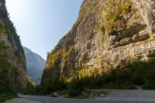 The road goes between the cliffs. Tourist car is parked at the curb of the road