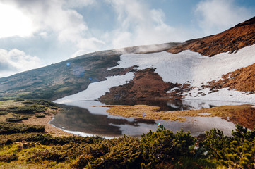 Beautiful spring scenery. Sunny morning in the mountains, melting snow on the slopes, reflection in the lake. Carpathian mountains, Ukraine