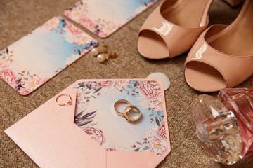 Wedding rings and engagement ring on wedding invitation near bridal shoes on high heels. Accessories for bride