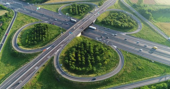 Cloverleaf interchange seen from above. Aerial view of highway road junction in the countryside with trees and cultivated fields. Bird's eye view.