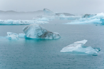 Drifting ice on a glacier lagoon in the rain, giving at bluish colour © Lux