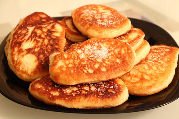 Pancakes sprinkled with sugar on a black plate. Pancakes with milk. Close-up.