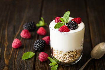 White yogurt with muesli and raspberries in glass bowls on rustic wooden background.