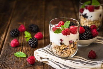 White yogurt with muesli and raspberries in glass bowls on rustic wooden background.