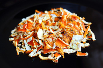 Finely chopped dried mandarin peel on a black plate. Isolated. Close-up.
