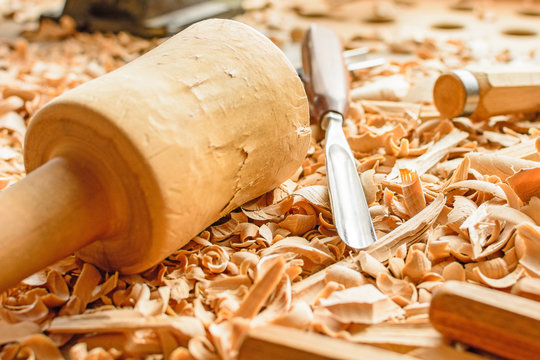Chisels laid in wooden shavings on the desk. Carving tools lying in the shavings. In a carving workshop. Cutting of linden wood. Wooden gavel on a work pontoon in a carving workshop.