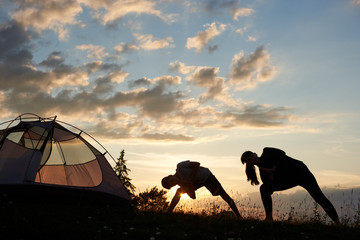 Yoga at mountains at the sunset. Family mam and son exercising and stretching outdoors near tent...