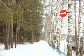 Winter road along the forest and pond. Sign Entry is forbidden hanging on a birch tree. Brick sign. Russia, February, 2018.