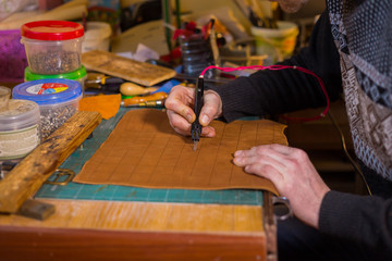 Professional male skinner, tanner making decorative details on leather playing field for strategy board game -tafl with special pyrographic machine