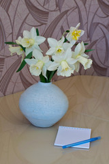 White daffodils in a vase on a table with with a notebook.