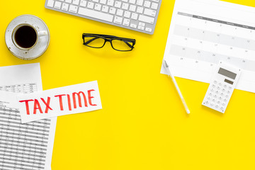 Tax time lettering on office work desk with calendar and bills on yellow background top view copy space