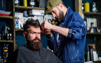 Hipster lifestyle concept. Barber with clipper trimming hair on temple of client. Hipster client getting haircut. Barber with hair clipper works on hairstyle for bearded man barbershop background