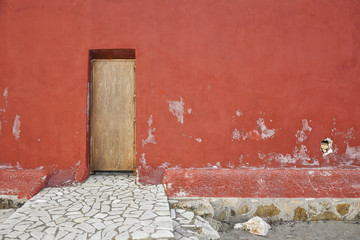 Exterior red wall with wooden doors and stone sidewalk. View on house from the outside with exit on the beach.