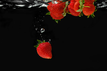 Strawberries falling into the water creating splashes.