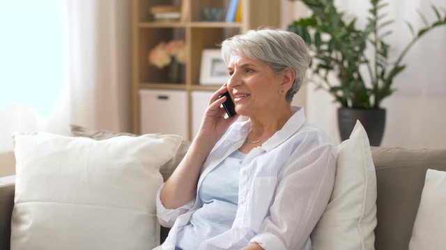 technology, communication and people concept - happy senior woman calling on smartphone at home