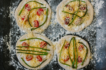 Cooking process of making mini pizza - small and personal, with cheese, tomatoes and asparagus.
