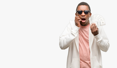 African man holding dollar bank notes terrified and nervous expressing anxiety and panic gesture, overwhelmed