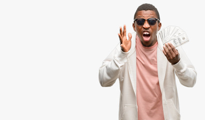 Naklejka premium African man holding dollar bank notes stressful keeping hands on head, terrified in panic, shouting