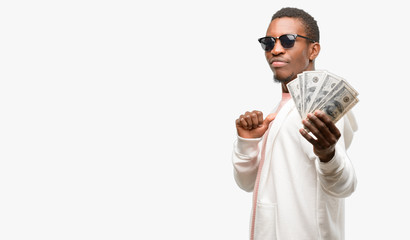 African man holding dollar bank notes proud, excited and arrogant, pointing with victory face