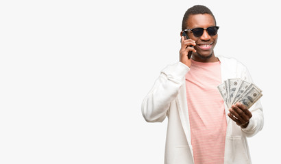Naklejka premium African man holding dollar bank notes happy talking using a smartphone mobile phone