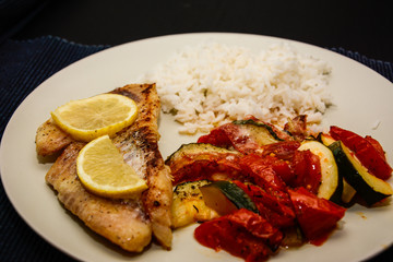 Fresh fish fried for dinner with lemon, rice pepper, tomato and oregano