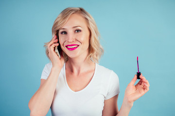 attractive and smiling woman blonde applies lipstick makeup pink fuchsia lips in the studio on a blue background