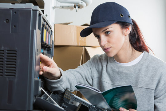 Lady with instruction book working on photocopier