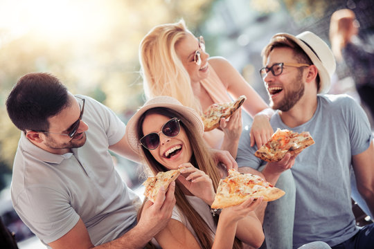 Close up of four young cheerful people eating pizza