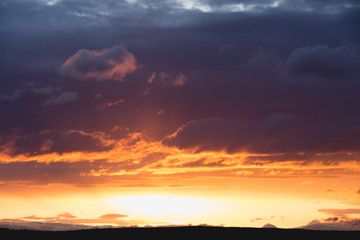 intensive clouds and golden sun beam at sunset horizon