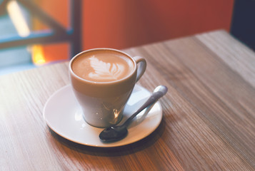 Cup of cappuccino at table. Cozy cafe interior. Latte art top view on wood table