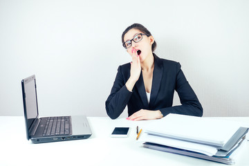 attractive displeased unhappy brunette businesswoman in a stylish business suit working in the office with a laptop and bored wants to sleep. concept of lack of sleep and deadline