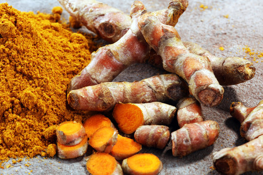 Turmeric powder and fresh turmeric on grey background