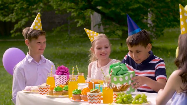 holidays, childhood and celebration concept - happy friends giving presents to birthday child at summer garden party