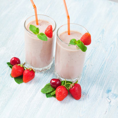 two glasses of smoothies made from milk, strawberries, banana, cherries, decorated with mint on bright white background Concept healthy lifestyle, diet, tasty Copy space